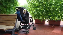 Детска количка с чанта на дръжката, паркирана до пейка в парка
